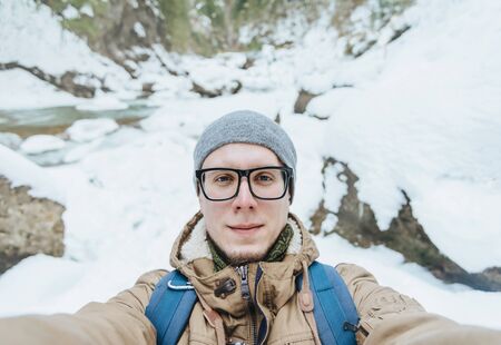 Traveler young man in glasses doing a self-portrait on background of winter nature, point of viewの写真素材