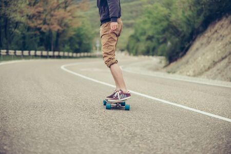 Unrecognizable young man riding on longboard on road in autumn outdoorの写真素材