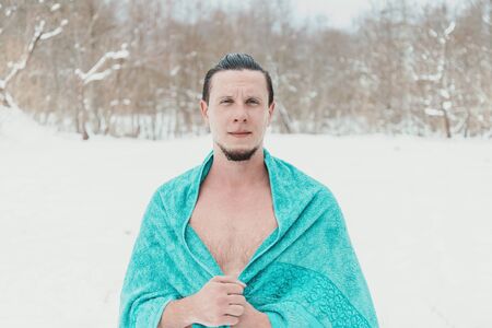 Young man standing with towel after swimming and hardening in winter to promote health, looking at cameraの写真素材