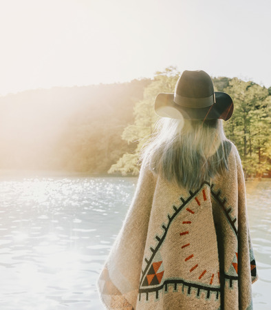 Boho style girl wearing in poncho and hat walking on lake, rear view.の写真素材