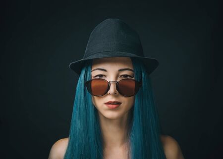 Portrait of fashionable beautiful young woman with blue hair in sunglasses and hat, looking at camera.の写真素材