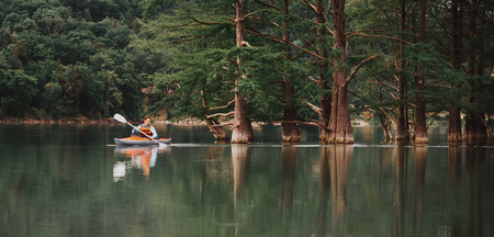 Traveler young man kayaking on lake Sukko on background of beautiful cypresses in summer, Anapa, Russia.の写真素材
