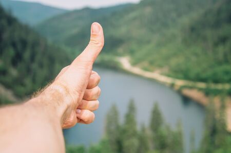 Traveler young man showing gesture thumb up on background of summer landscape, point of view shot.の写真素材