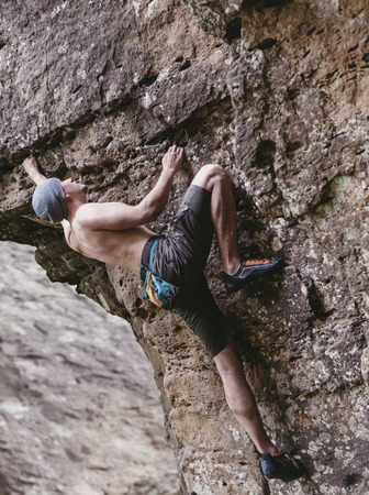 Sporty shirtless young man free climbing on rock outdoor.の写真素材