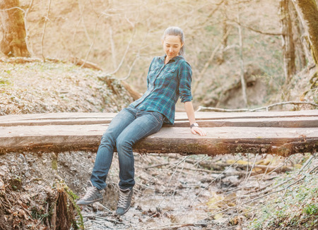 Young woman sitting on wooden bridge over the river in spring forest.の写真素材