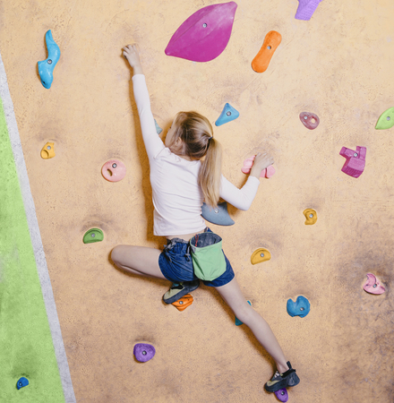 Little girl free climbing on artificial wall in gym, bouldering.の写真素材