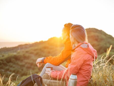 Traveler young couple resting in summer mountains at sunset and enjoying view of nature.の写真素材