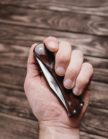 Male hand holding stainless jackknife on a wooden background.の写真素材