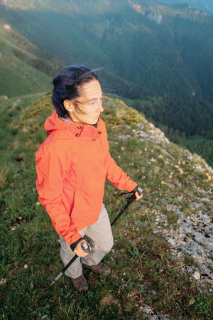 Hiker young woman walking with trekking poles in summer mountains in windy weather.の写真素材
