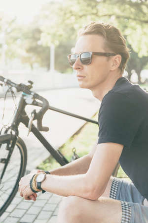 Handsome cyclist young man in sunglasses rests in summer park.の写真素材