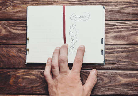 Unrecognizable man opens to do note on a wooden table, view of hand.の写真素材
