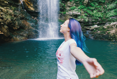 Freedom happy young woman standing with raised arms near the waterfall in summer, side view.の写真素材