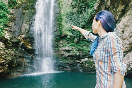 Explorer young woman pointing at waterfall in summer.の写真素材