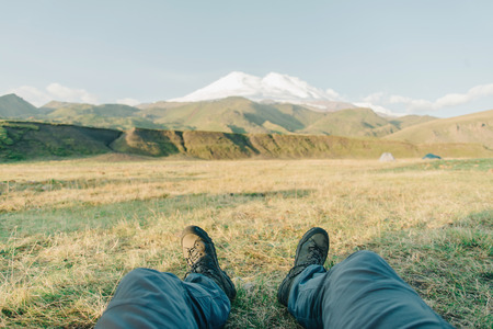 Hiker young man sitting in front of mountain Elbrus in summer, point of view.の写真素材