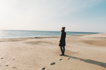 Young woman walking on sandy shore and enjoying view of sea in autumn.の写真素材