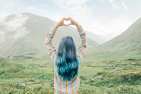 Young woman standing in summer mountains and making heart shape with her hands.の写真素材