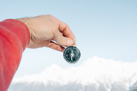 Male hand holding compass on background of snowy mountains, point of view.の写真素材