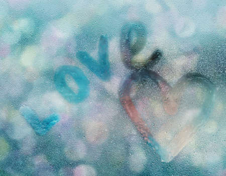 Heart shape and word love written on glass with water drops in rainy weather in front of defocused city lights.の写真素材