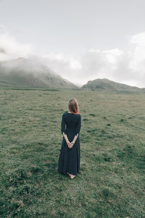 Young woman wearing in long dress walking in summer mountains, rear view.の写真素材