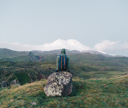 Far away in the mountains in the Caucasus a man sits a stone and admires Mount Elbrusの写真素材