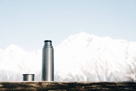 Bottle with cup on a wooden table on background of snowy mountains in winter.の写真素材