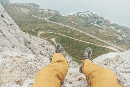 Man sitting on edge of cliff over coastline, view of legs, pov.の写真素材