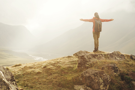 Explorer young woman with backpack standing with raised arms in the mountains at sunset.の写真素材