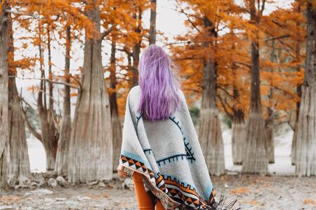 Unrecognizable young woman with violet hair wearing in poncho walking in autumn park.の写真素材