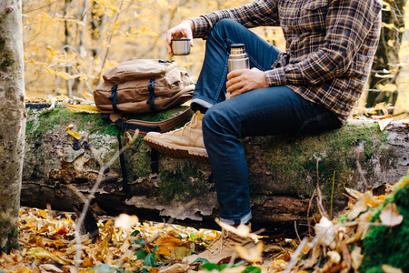 Unrecognizable young man resting with cup of tea in autumn forest.の写真素材