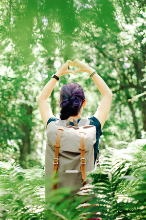 Backpacker young woman standing in summer forest and making heart shape with her hands.の写真素材