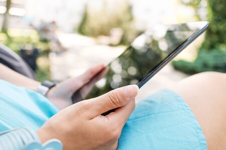 Unrecognizable young woman using digital tablet in the park, close-up of hands.の写真素材