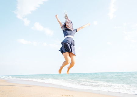 Happy young woman jumping on sand beach near the sea, summer vacations.の写真素材