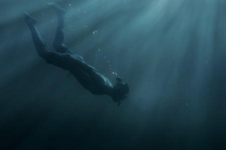 Young man freediver swimming with mask and snorkel underwater in deep sea among sunbeams.の写真素材