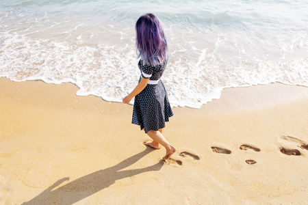 Unrecognizable barefoot young woman walking on beach leaving footprints in the sand near sea. Summer vacations.の写真素材