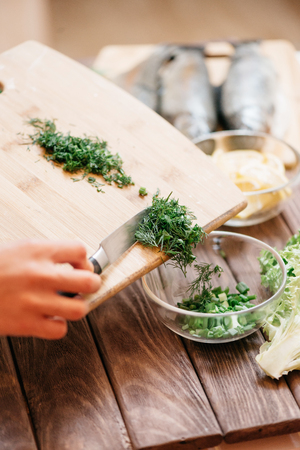 Womanâs hands pours sliced greenery from board into a plate in the kitchen.の写真素材