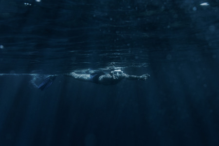 Young man wearing in mask with snorkel and flippers swimming underwater surface sea.の写真素材