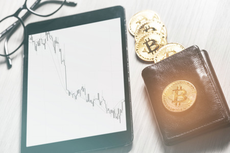 Symbol of virtual money - bitcoins on purse and digital tablet with financial diagram, business workspace.の写真素材