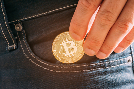 Hand putting bitcoin into pocket, symbol of crypto currency and virtual money, close-up.の写真素材