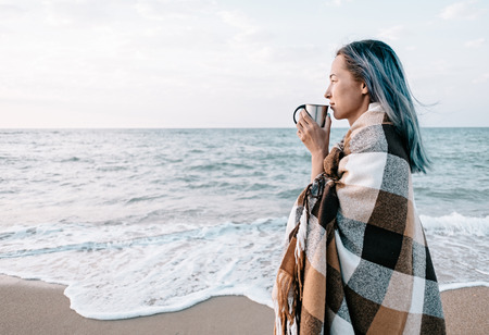 Beautiful young woman relaxing with cup of drink on sand coast near the sea, beach vacations.の写真素材