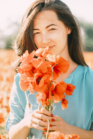 Portrait of smiling beautiful young woman with bouquet of poppies outdoor, looking at camera.の写真素材