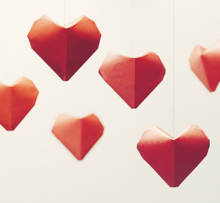 Many red paper origami hearts, symbol of love, on white background. Greeting card on Valentines day.