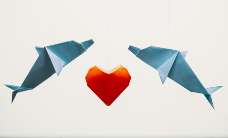 Two origami dolphin around red paper heart on white background. Greeting card for Valentines day.の写真素材