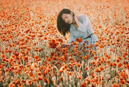 Romantic beautiful young woman walking in summer poppy flower field.の写真素材