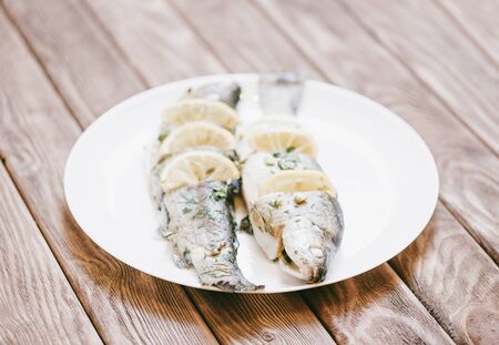 Fish trout dish with lemons and greenery on a white plate on wooden table.の写真素材