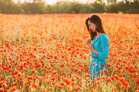 Dreamy romantic beautiful young woman smelling a red poppy in flower meadow in summer.の写真素材