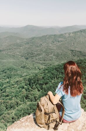 Unrecognizable hiker young woman with backpack resting on top of rock in front of summer mountains.の写真素材