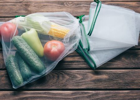 Fresh vegetables in reusable eco bag near empty mesh package on a wooden background, top view. Zero waste and no plastic concept.の写真素材