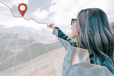 Explorer young woman pointing at mountain peak with location pin and track. Navigation concept.の写真素材