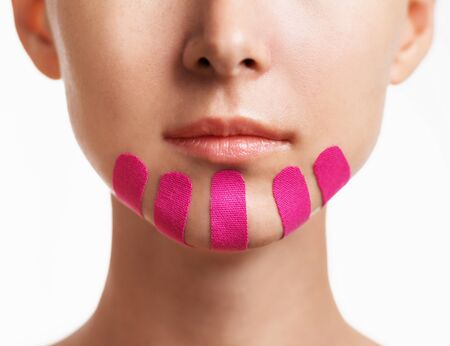 Young woman with vertical kinesio tapes on chin for facelift, front view. Anti-aging and beauty procedure.の写真素材