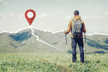 Hiker backpacker young man with trekking poles standing in front of route with location GPS pin on peak of mountain ridge in summer outdoor.の写真素材
